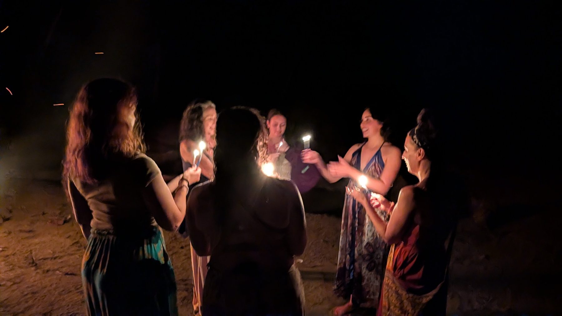 Retreat guests holding candles in a circle on the beach at night