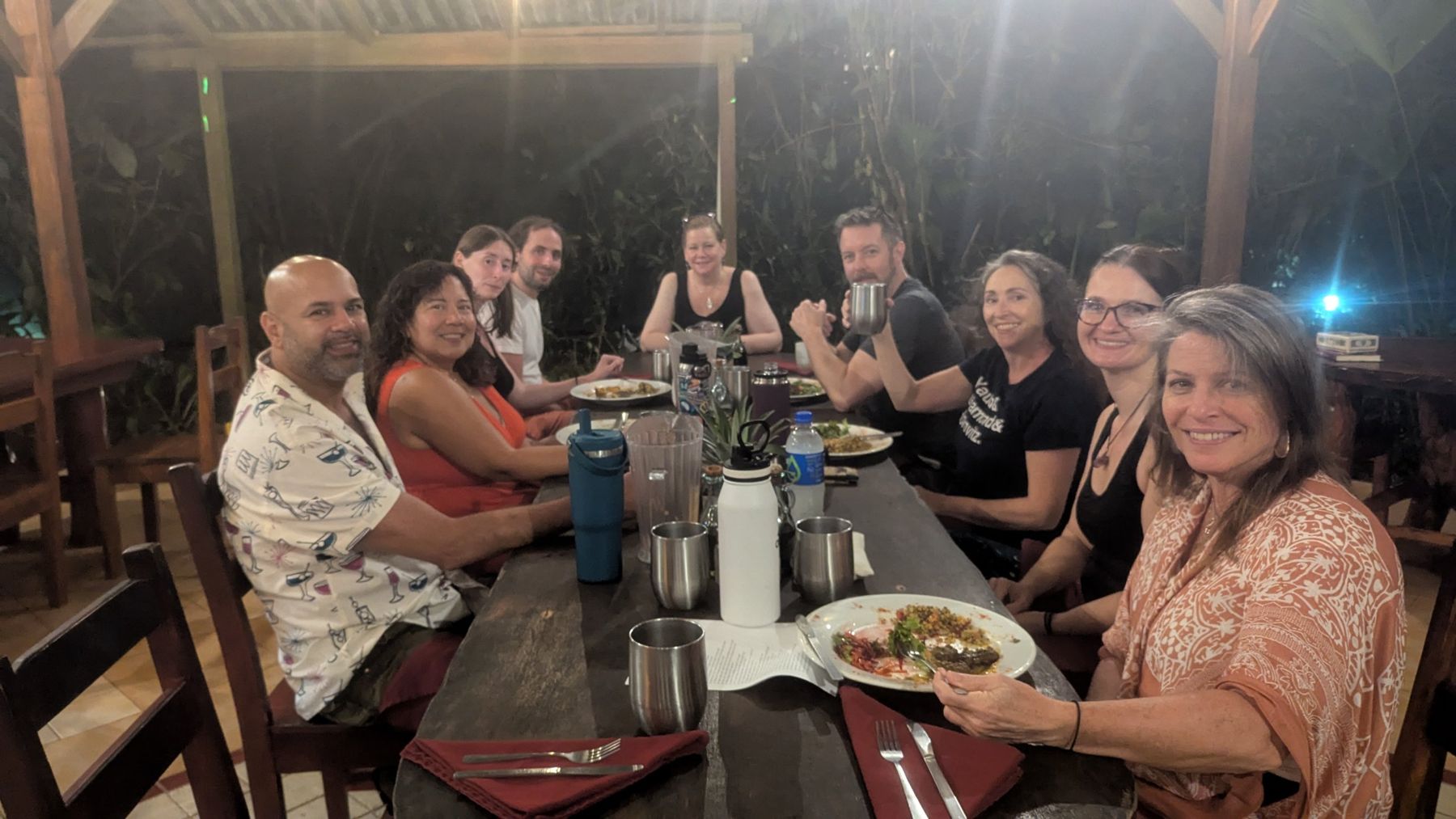 Retreat guests smiling around a long dinner table in an open-air jungle pavilion
