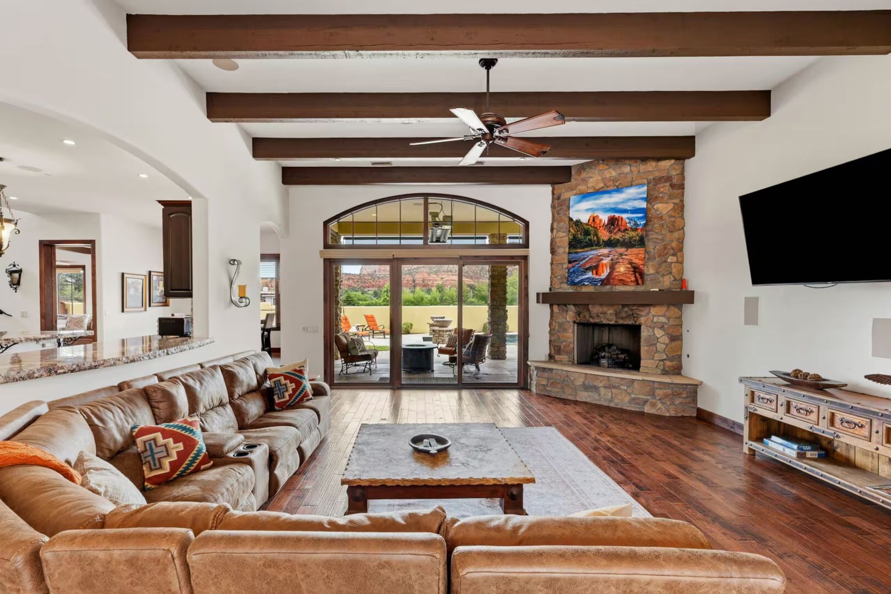 Spacious living room with leather sectional, beamed ceiling and stone fireplace